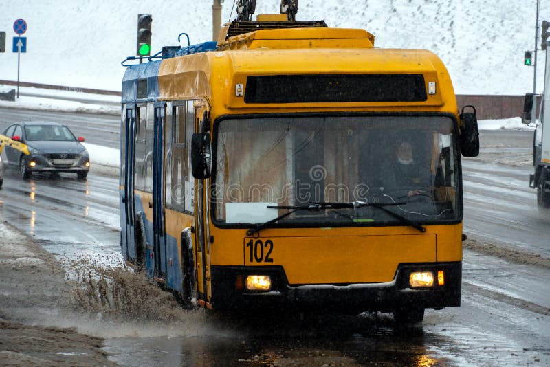 Grodno, Belarus, February 9, 2022: Passing cars in a large puddle during rain and sleet. Large splashes from under the wheels of