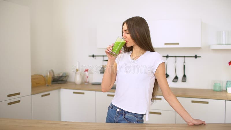 Groene detox smoothie - gezonde vrouw die plantaardige smoothie drinken Gelukkige jonge vrouw die het verse groene sap genieten d