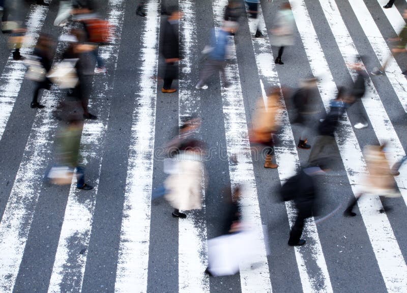Group of pedestrians crossing the street at a zebra crossing with motion blur to the people and focus to the markings on the road, high angle view. Group of pedestrians crossing the street at a zebra crossing with motion blur to the people and focus to the markings on the road, high angle view