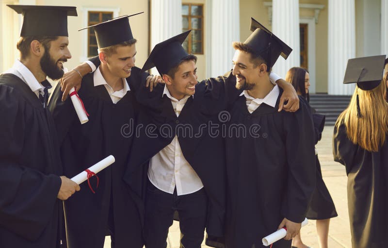 Group of happy boys students university graduates mates standing and hugging with diplomas in hands over university building at background. Graduation from university, education, diploma concept. Group of happy boys students university graduates mates standing and hugging with diplomas in hands over university building at background. Graduation from university, education, diploma concept