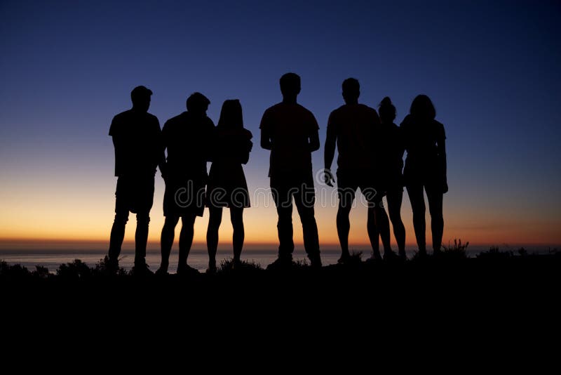 Groep jonge volwassenen die zonsondergang bewonderen door de kust