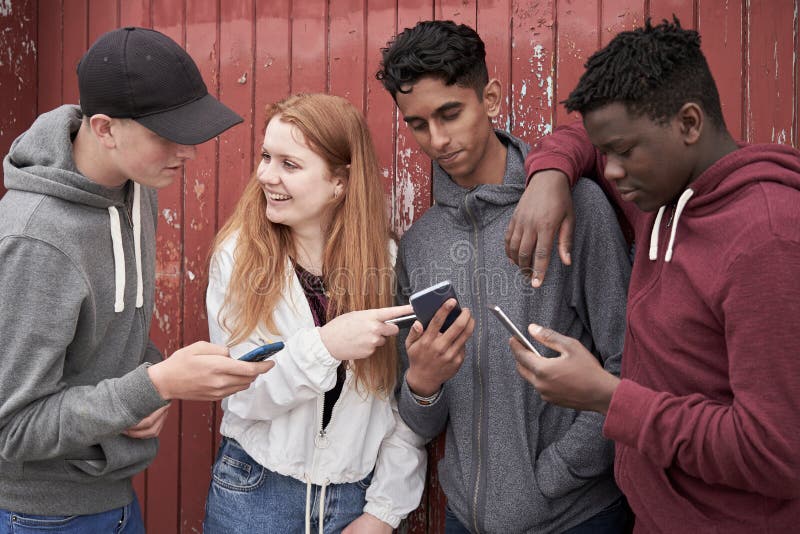 Groep Tienervrienden die Mobiele Telefoons in het Stedelijke Plaatsen bekijken stock foto Groep Tienervrienden die Mobiele Telefoons in het Stedelijke Plaatsen bekijken stock foto