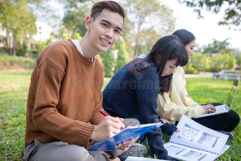 Groep Universitaire Studenten Aziatische zitting op het groene gras die en buiten in een park samenwerken lezen royalty-vrije stock foto Groep Universitaire Studenten Aziatische zitting op het groene gras die en buiten in een park samenwerken lezen royalty-vrije stock foto