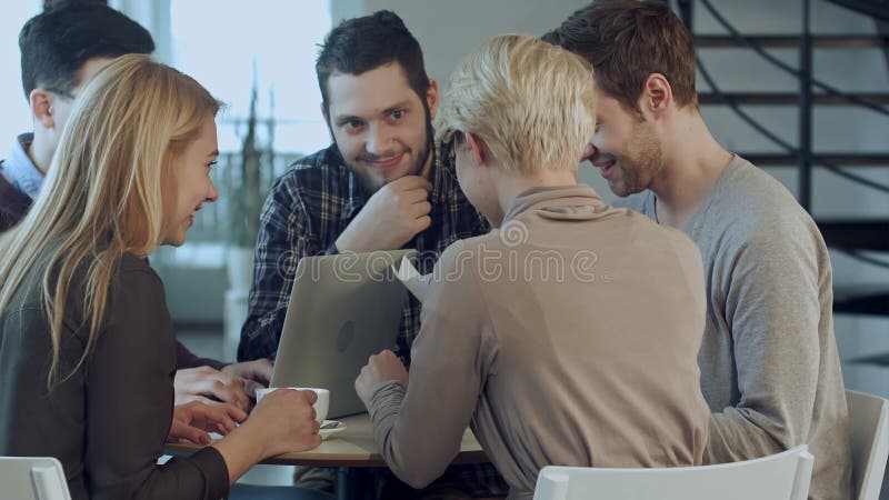 Groep van vijf mensen die iets bespreken met glimlach terwijl het zitten bij de bureaulijst