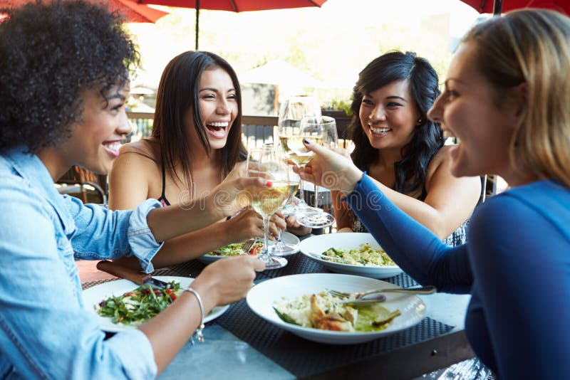 Groep Vrouwelijke Vrienden die van Maaltijd genieten bij Openluchtrestaurant stock foto Groep Vrouwelijke Vrienden die van Maaltijd genieten bij Openluchtrestaurant stock foto