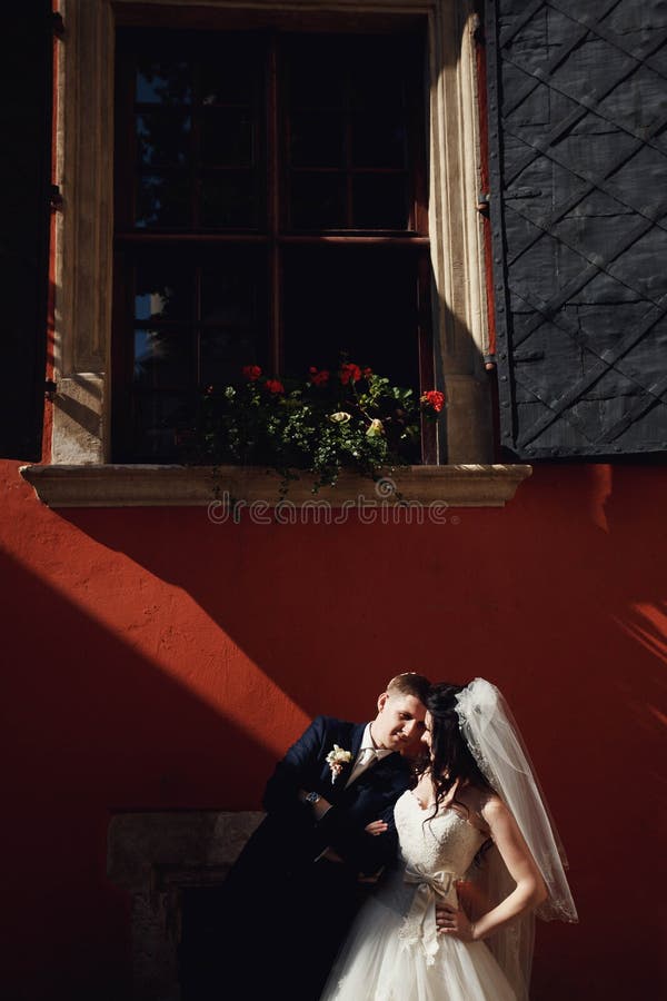 Grom che huging baciando sposa con capelli rossi vicino alla parete all'aperto Leopoli fotografia stock Grom che huging baciando sposa con capelli rossi vicino alla parete all'aperto Leopoli fotografia stock
