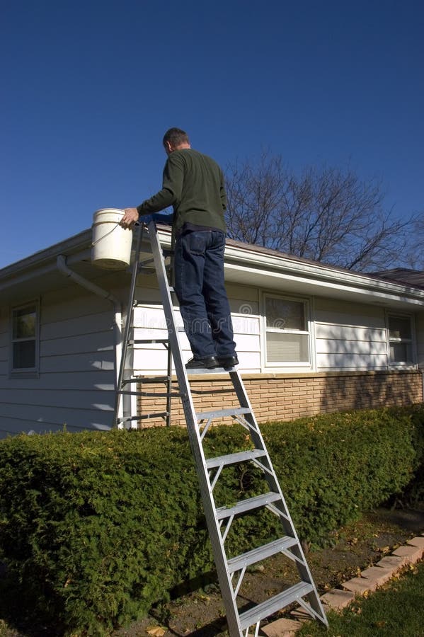 Man performing home maintenance, inspecting house roof and cleaning rain gutters while up on a ladder. Man performing home maintenance, inspecting house roof and cleaning rain gutters while up on a ladder.