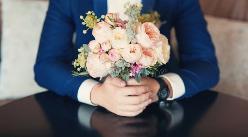 A groom with bridal wedding peony bouquet in his hands