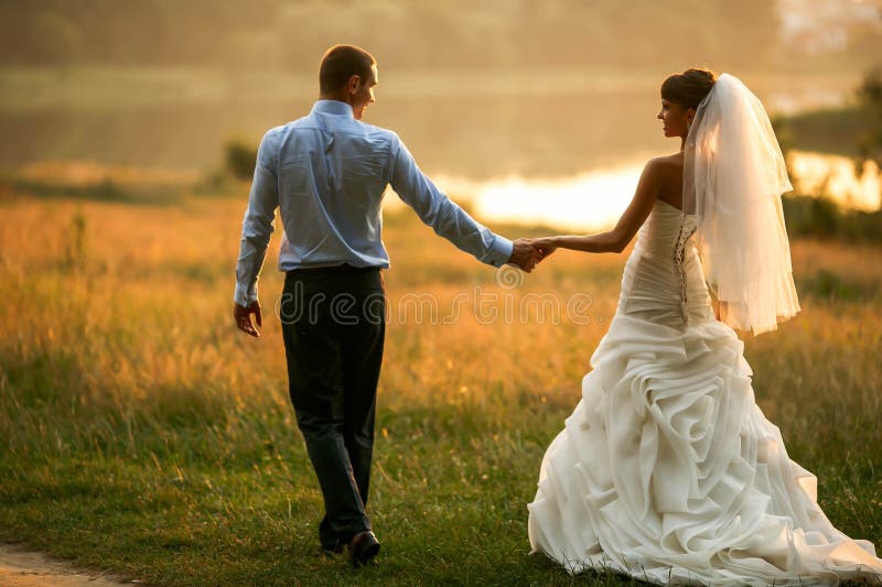 Groom and bride are holding hands on the background green forest