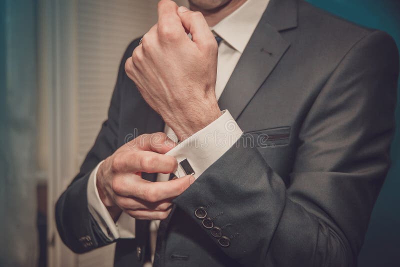 Groom clasps cuff links on a shirt sleeve close up