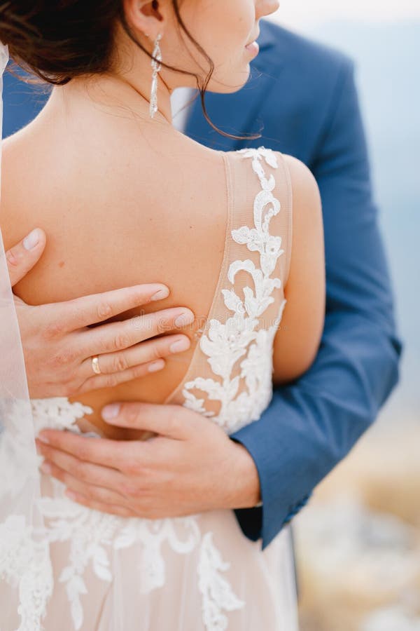 The groom gently hugs the bride and strokes her back with his hands, close-up