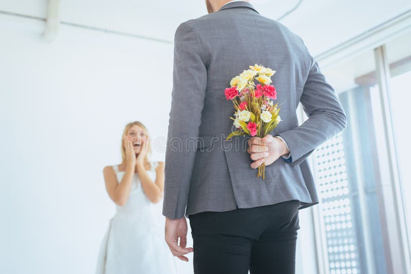 Groom hiding flower behind back in order to surprised bride on the wedding day,Woman positive emotion and face astonished happy an