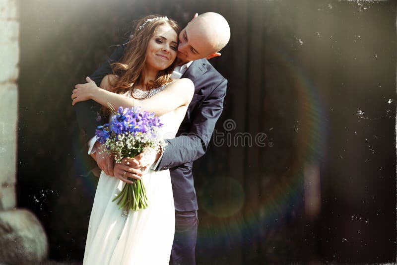 Groom kisses bride's cheek hugging her from behind in the rays o royalty free stock image