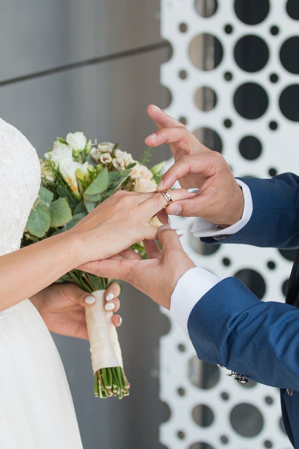 The groom places the ring on the bride& x27;s hand. Photo closeup. Boutonniere, engagement.