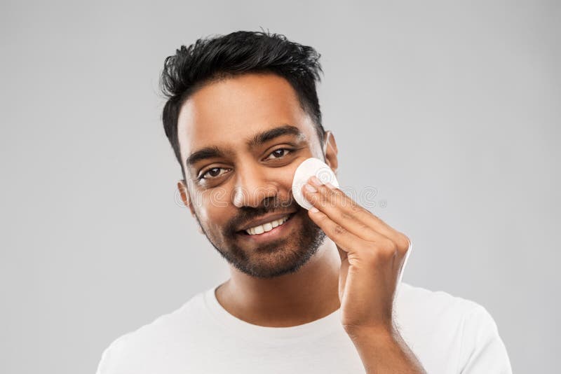 Smiling indian man cleaning face with cotton pad
