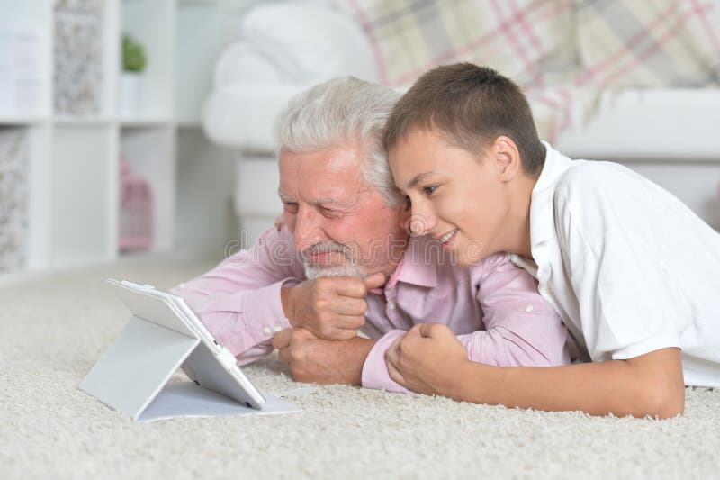 Grootvader met kleinzoon die laptop gebruikt terwijl hij op de vloer ligt