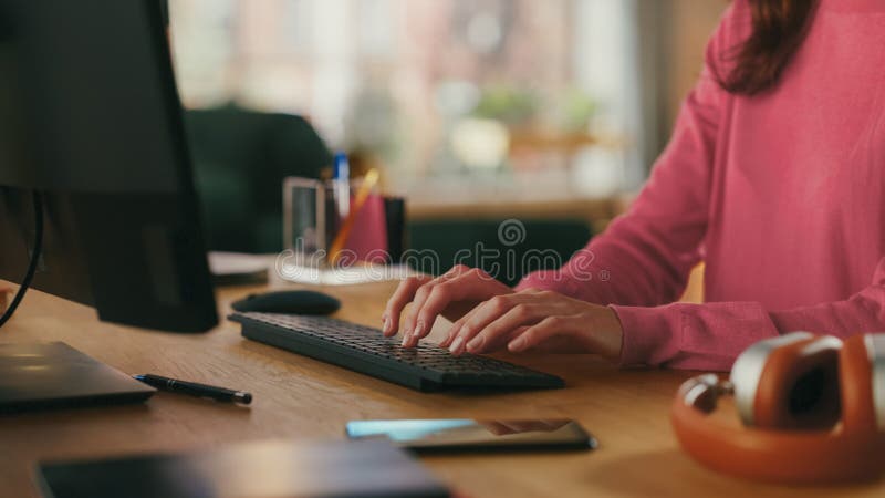 Close Up of a Female in Pink Jumper Working from Home on Desktop Computer. Student Making Homework Assignment, Studying for School Exams. Loft Apartment with Urban City View from Big Window. Close Up of a Female in Pink Jumper Working from Home on Desktop Computer. Student Making Homework Assignment, Studying for School Exams. Loft Apartment with Urban City View from Big Window.