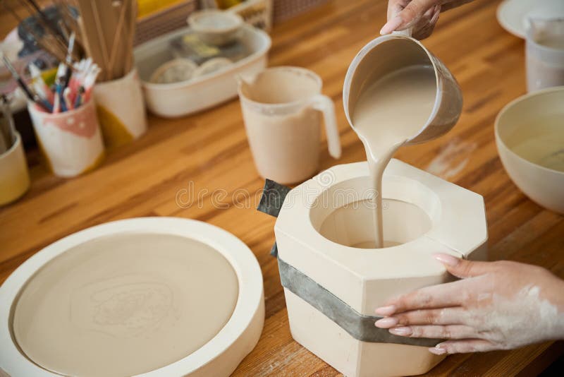Gros plan des mains femelles coulant le mélange de poterie dans le moule pour la mug photographie stock