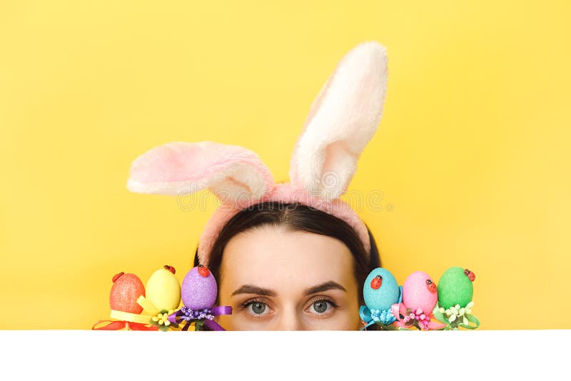 Gros plan portrait d'une jeune femme amusante porte des oreilles lapin cache visage près des oeufs de Pâques regarde mystérieuseme image libre de droits