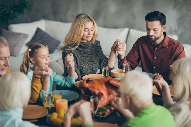 Grote familieleden die op de tafel van de feestdag zitten, genieten van een oktober-maaltijd en bidden dat ze volwassen familiele