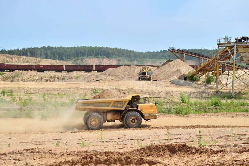 Grote gele stortplaatsvrachtwagen die zand in een dagbouwmijnbouwsteengroeve vervoeren