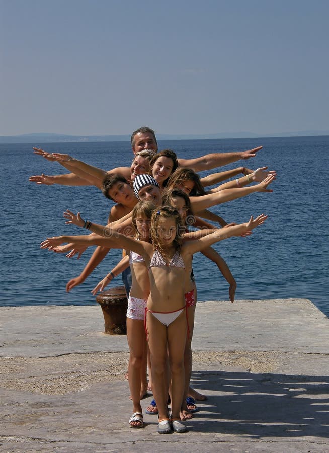 Big happy smiling family (best friends) together sending greetings from port at the Adriatic sea in Croatia (Dalmatia) at sunny day. They are happy and keep arms in air like a dancing and singing on old pier. Vertical photo. Big happy smiling family (best friends) together sending greetings from port at the Adriatic sea in Croatia (Dalmatia) at sunny day. They are happy and keep arms in air like a dancing and singing on old pier. Vertical photo.