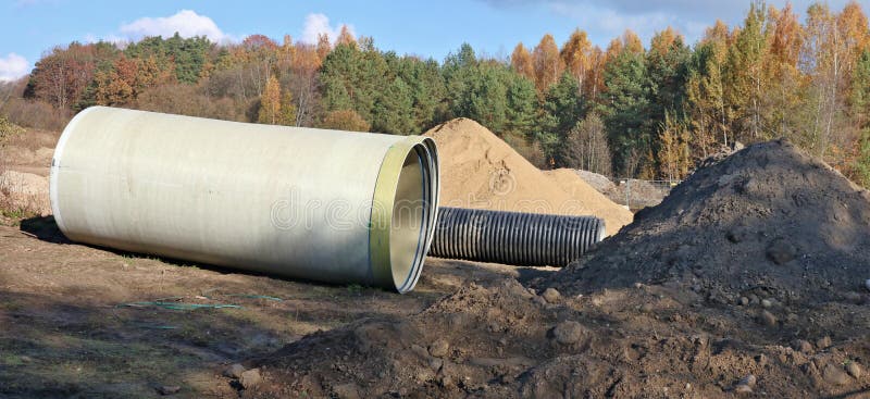 Grote rioolpijpen en stapel van zand in een de herfstbos const stock afbeelding Grote rioolpijpen en stapel van zand in een de herfstbos const stock afbeelding