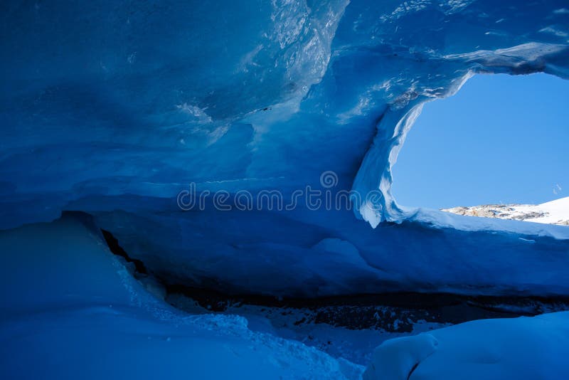 Grotte de glace bleue avec lumière vive qui s'infiltre à travers le plafond. De l'intérieur d'une grotte de glace un ciel bleu frappant est visible à travers l'ouverture du plafond