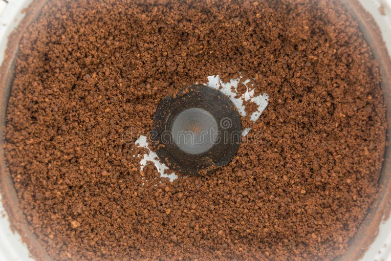 Ground grilled dark coffee beans in an automatic coffee grinder, close-up of food background