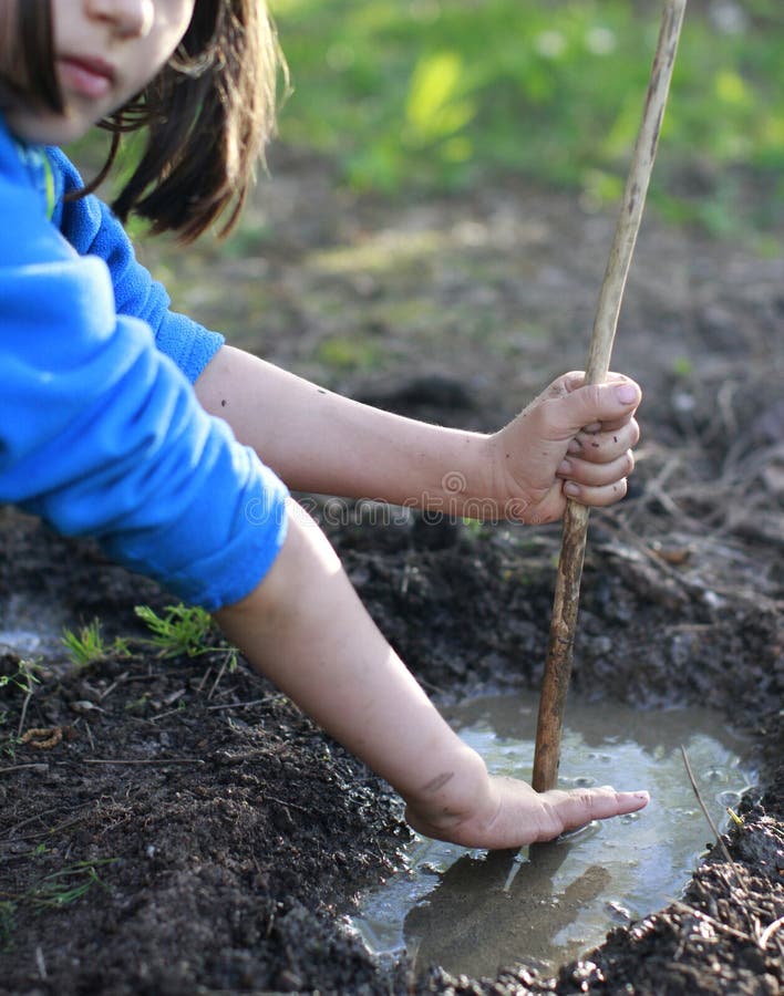 Grounded child playing with mud and stick for nature discovery