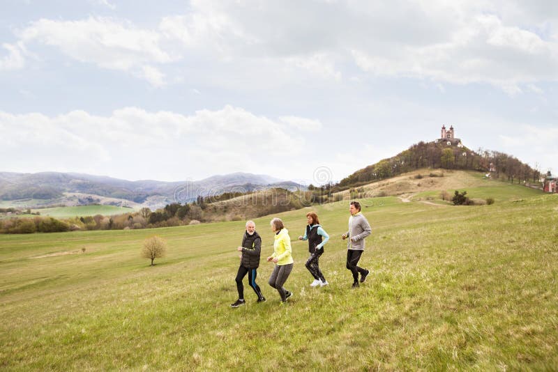 Skupina seniorov bežiacich vonku na zelených kopcoch.
