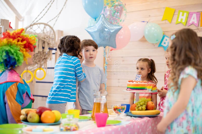 Group of adorable kids stand around festive table at birthday party stock photos Group of adorable kids stand around festive table at birthday party stock photos
