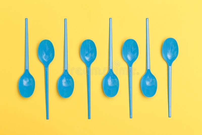 Group of Blue Disposable Plastic Spoons Over a Yellow Background Stock