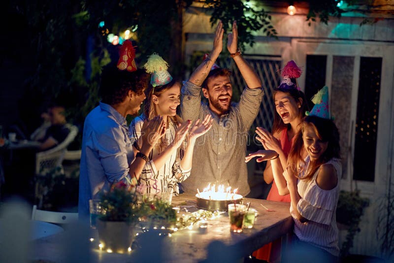 Group of cheerful friends wishing happy birthday to female friend at the open air party on a beautiful summer night. Quality friendship time together. Group of cheerful friends wishing happy birthday to female friend at the open air party on a beautiful summer night. Quality friendship time together