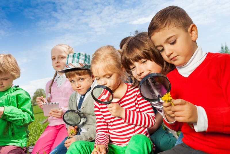 Group of children sitting in field with magnifier royalty free stock photos