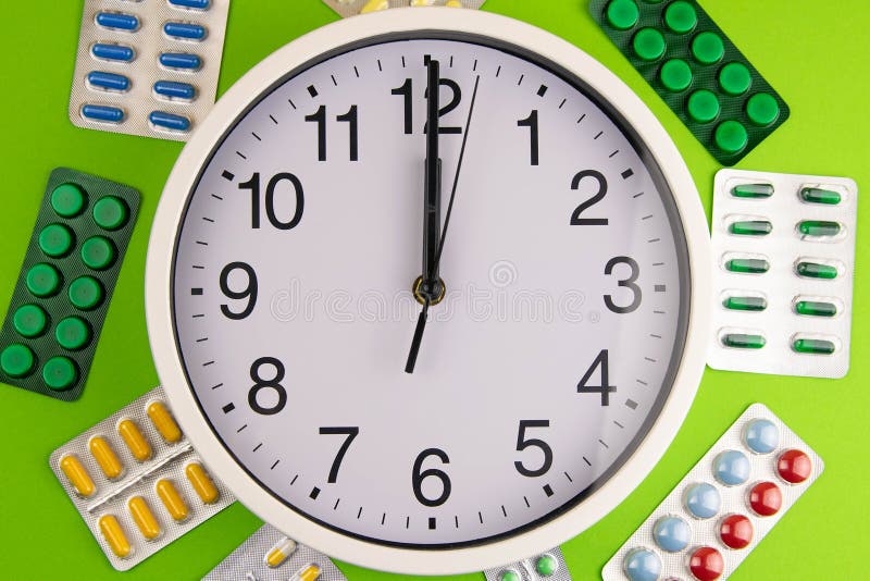 Group of different pills arranged in shape of circle Inside are the clock on green background royalty free stock images