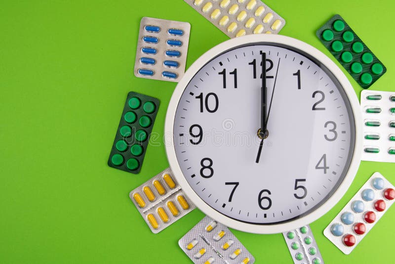 Group of different pills arranged in shape of circle Inside are the clock on green background stock image