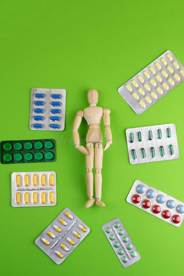 Group of different pills arranged in shape of circle Inside wooden figurine of a man on green background. Top views with clear space
