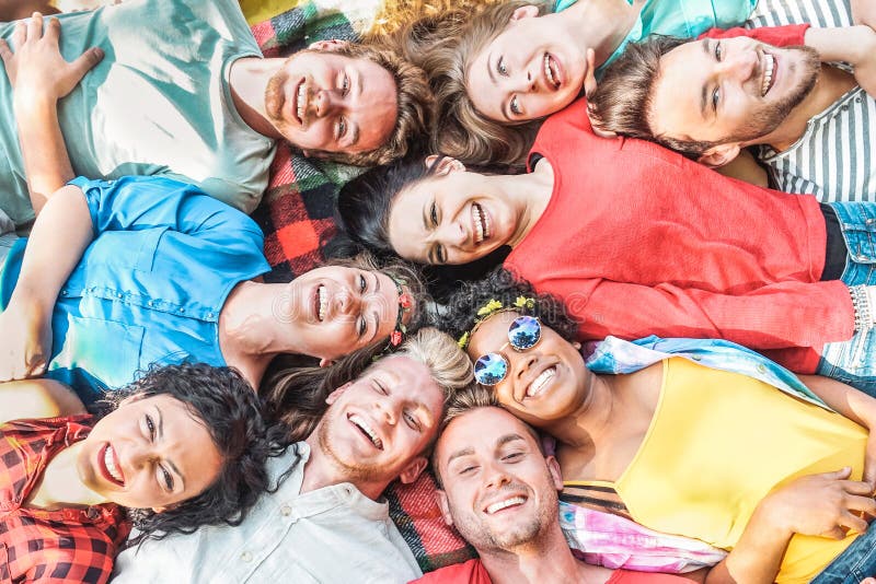 Group of diverse friends having fun outdoor - Happy young people lying on grass after picnic and laughing together