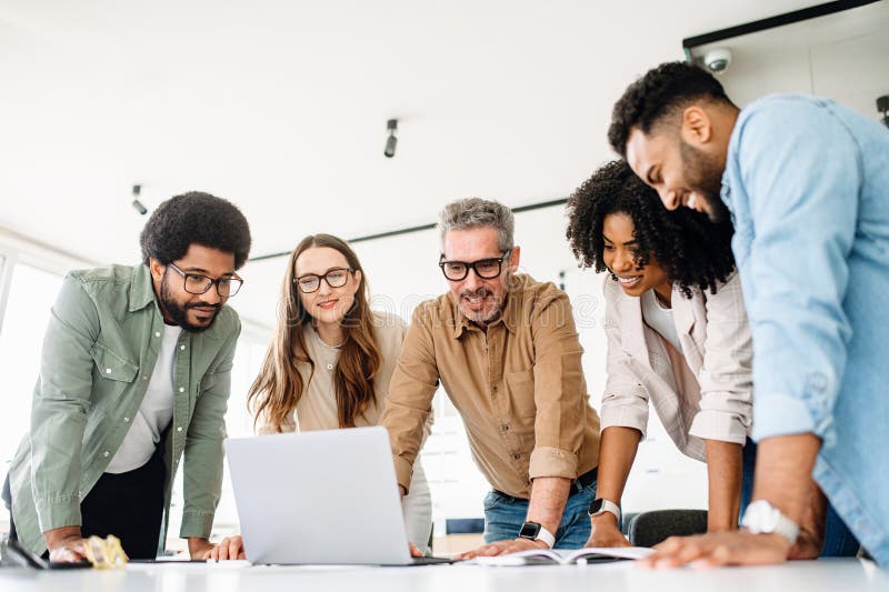 A group of diverse professionals is standing around a laptop, highlighting a moment of team collaboration stock images