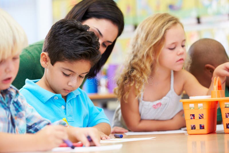 Group Of Elementary Age Children In Art Class With Teacher Drawing On A Piece Of Paper