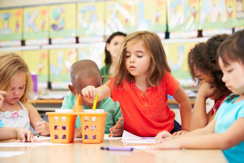 Group Of Elementary Age Children In Art Class With Teacher Reaching For Crayon