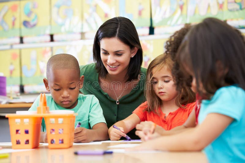 Group Of Elementary Age Children In Art Class With Teacher Sitting At Table