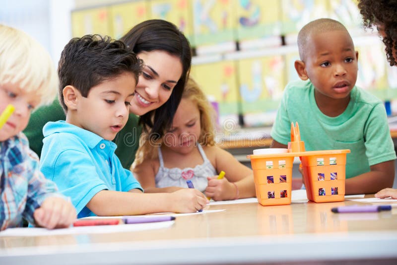 Group Of Elementary Age Children In Art Class With Teacher Sitting At Table Chatting