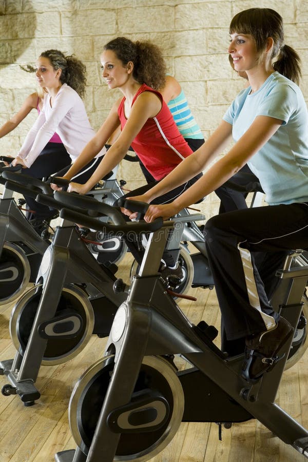 The group of women training on exercise bikes at the gym. Side view. The group of women training on exercise bikes at the gym. Side view.