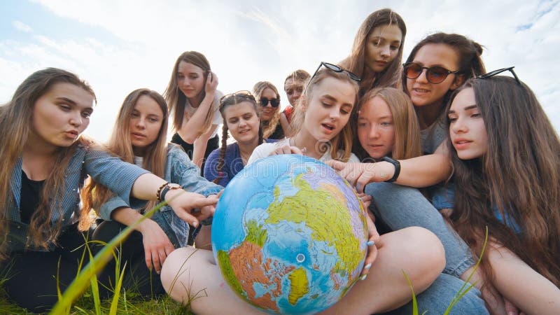 A group of female students are sitting in a meadow and studying the globe of the world. royalty free stock photo