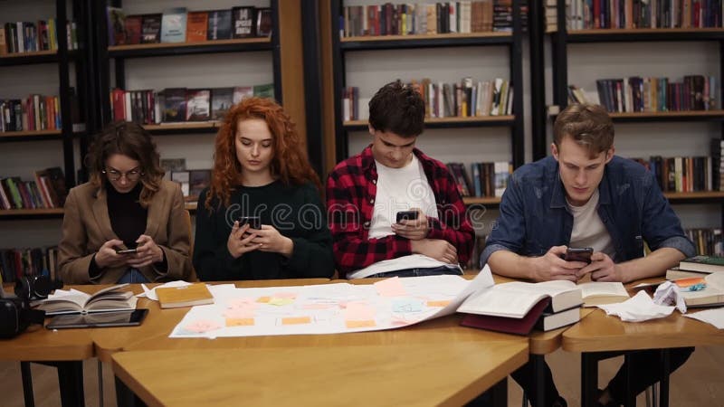 Group of four university students two males, two females sitting at the table together during break and using