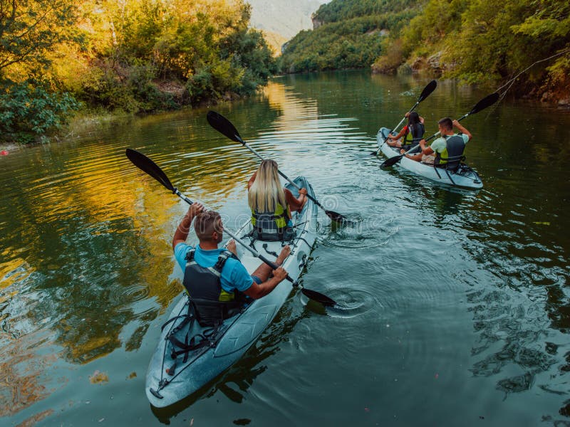 A group of friends enjoying having fun and kayaking while exploring the calm river, surrounding forest and large natural stock image