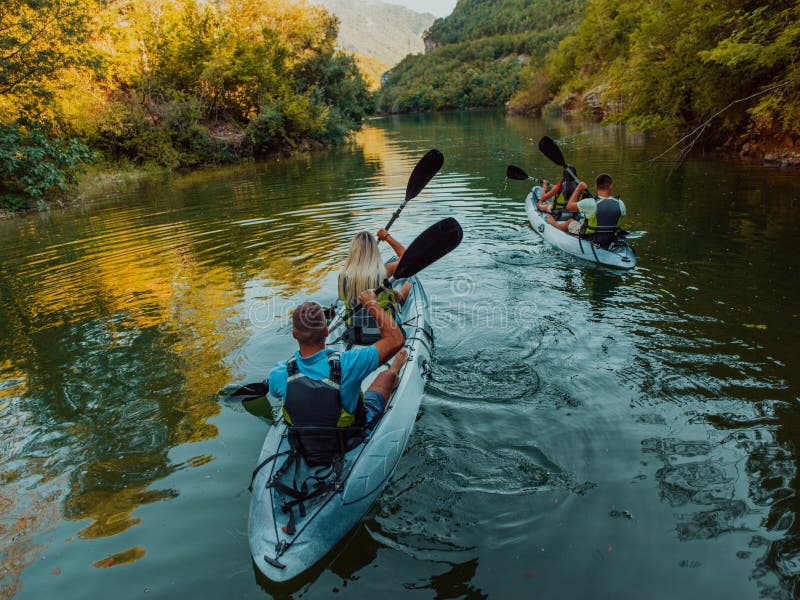 A group of friends enjoying having fun and kayaking while exploring the calm river, surrounding forest and large natural stock image