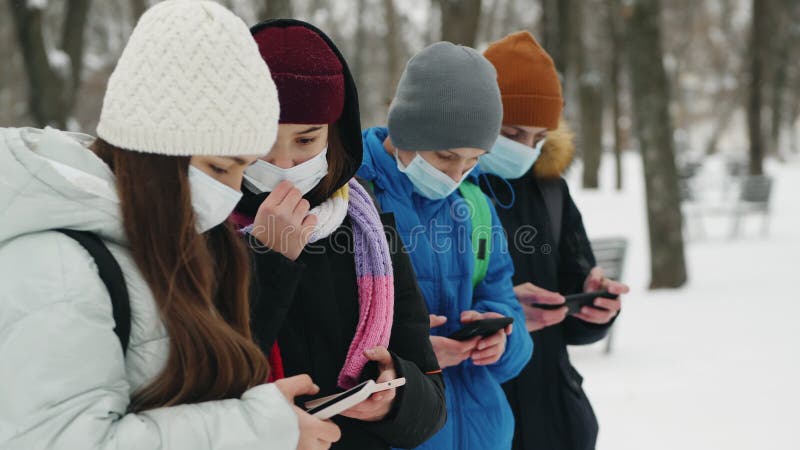 A group of friends in masks hold smartphones in their hands in the winter season